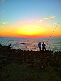 Silhouette people standing on beach against sky during sunset