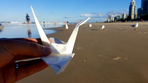 Close-up of hand holding paper crane at beach