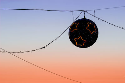 Low angle view of lighting equipment hanging against sky during sunset