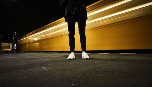 Low section of man standing on road at night