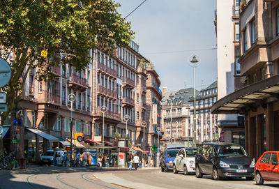 Cars on city street by buildings against sky