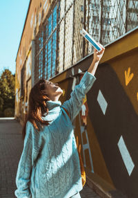 Young woman holding umbrella standing against built structure