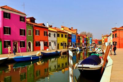 Boats moored in canal by buildings against sky