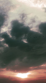 Low angle view of silhouette birds flying against dramatic sky