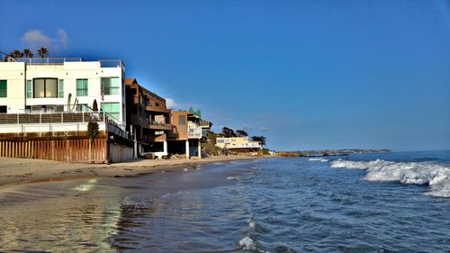 Houses by sea against clear blue sky