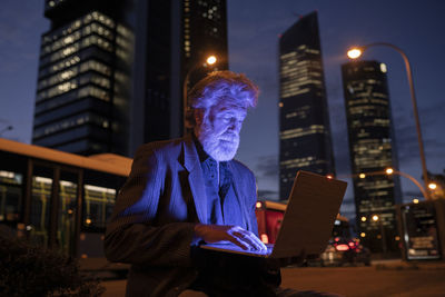 Man using mobile phone against illuminated buildings in city at night