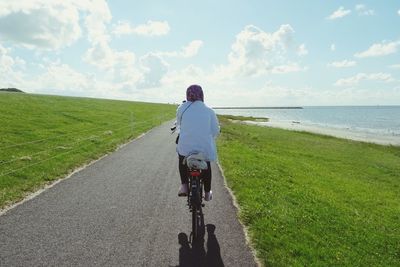 Rear view of woman riding bicycle on road by sea