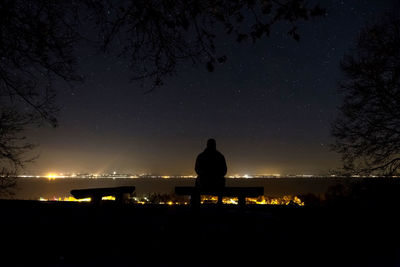 Silhouette of man sitting against sky at night