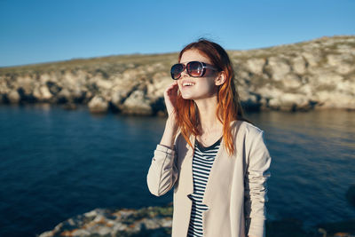 Young woman wearing sunglasses standing against sea