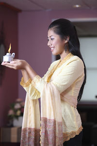 Young woman holding oil lamp while standing at home