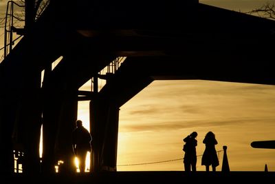 Silhouette people standing by sea against sky during sunset