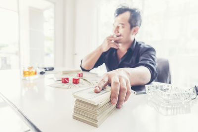 Thoughtful businessman with money and dices at desk in office