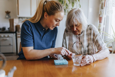 Female caregiver assisting senior woman while taking medicines at home