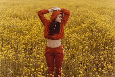 Young woman with arms raised standing amidst flowers on field
