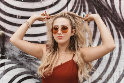 Young woman wearing sunglasses while standing against graffiti wall