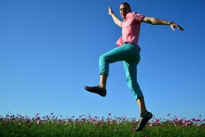 Portrait of happy man jumping over flowering field against clear blue sky