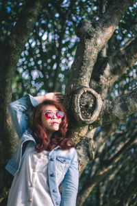 Portrait of woman standing by tree trunk in forest