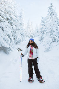 Full body glad woman in outerwear with stick and snowshoes standing on snowy path near spruces on winter day in valley of the ghosts in monts valin national park in quebec, canada