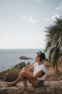 Man sitting at beach against sky