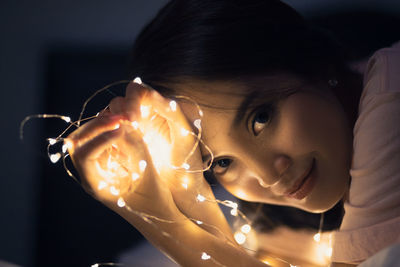 Close-up portrait of young woman holding illuminated string light