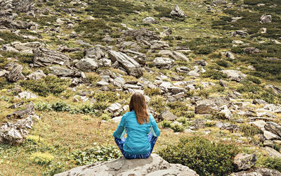 Rear view of woman in blue sitting on rock in meditation , mountain landscape relaxation nature yoga