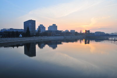 Reflection of buildings in river against sky during sunset