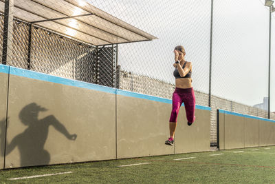 Full body of enduring female athlete in activewear jumping above ground during intense training in stadium