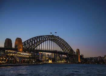 Illuminated bridge over river against clear sky at sunset