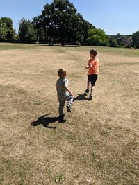 Rear view of siblings running on field during sunny day