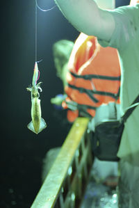 Cropped hand of man showing fish while standing outdoors at night