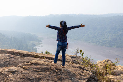 An woman with outstretched hands standing on hill top facing backside and enjoying nature