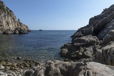 Scenic view of sea and rocks against clear blue sky