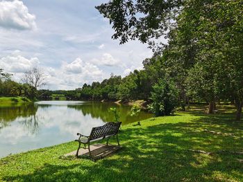 Empty bench in park by lake against sky