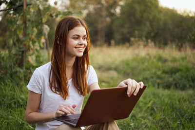 Young woman using laptop while sitting on field