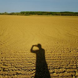 Shadow of man on sand on field against sky