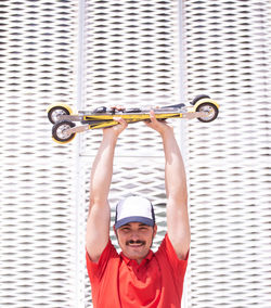 Portrait of smiling man lifting ski roller against metallic structure