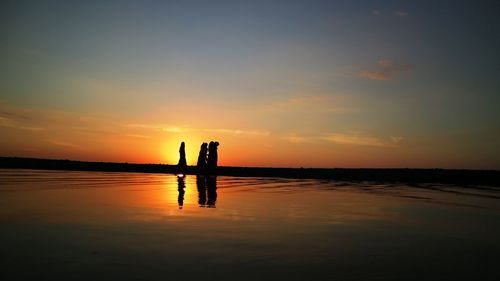 Silhouette people standing by sea against sky during sunset