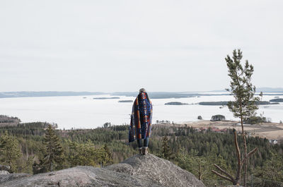 Woman wrapped in a blanket looking at the view of the ocean and forest