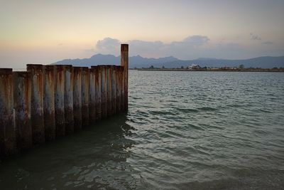 Old groyne in sea against sky during sunset