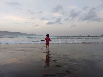 Rear view of boy on beach against sky