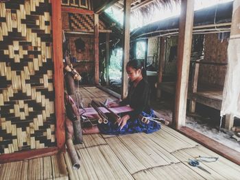 Side view of young woman weaving wool at home