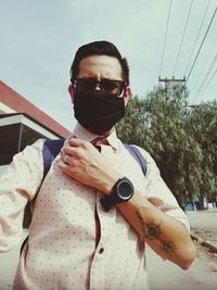 Portrait of young man holding sunglasses against sky