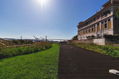 Footpath by canal against sky on sunny day