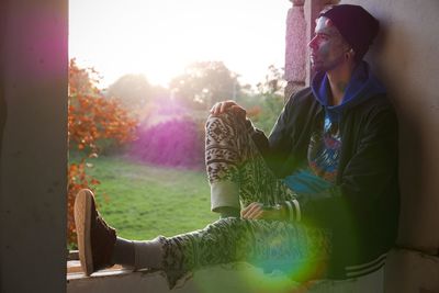 Hipster sitting on window sill while looking away