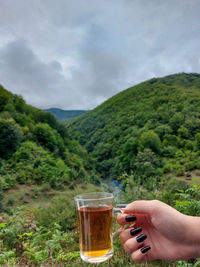 Midsection of woman drinking glass on table against mountains