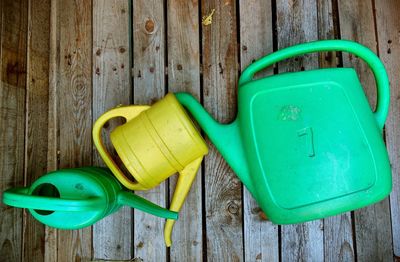 Directly above shot of green and yellow watering cans on floorboard