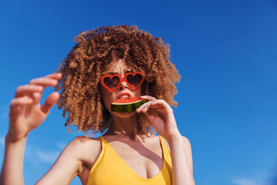 Young woman wearing sunglasses against clear blue sky