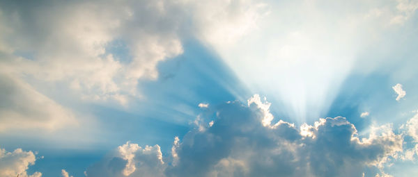 Low angle view of sunlight streaming through clouds