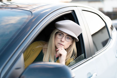 Middle-aged thoughtful woman driver driving a car. female with hat and glasses, transport concept