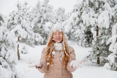 Portrait of smiling woman standing on snow covered trees during winter